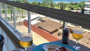 A balcony with a table set for two, featuring a plate of food, two glasses of beer, and a can of beer.