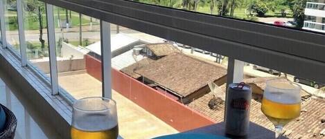 A balcony with a table set for two, featuring a plate of food, two glasses of beer, and a can of beer.