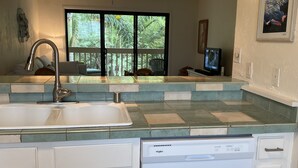 A kitchen with a dishwasher, white cabinets, a window with a view of greenery, and a ceiling fan.
