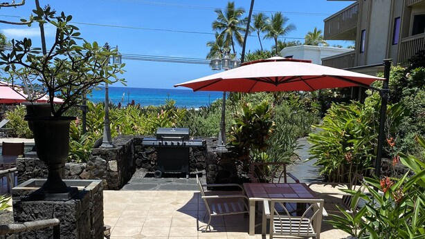 A patio area with a grill, outdoor seating, and a view of the ocean.