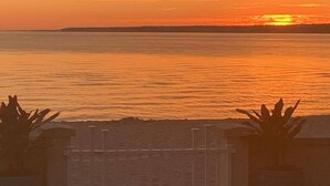 A sunset over a calm sea with a distant shoreline. - 3BR Beachfront Getaway – Behind Owner’s Home (Sylvan Beach)