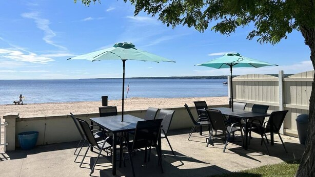 An outdoor patio with tables and chairs, two umbrellas, and a view of the beach and ocean. - 3BR Beachfront Getaway – Behind Owner’s Home (Sylvan Beach)