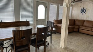 A dining area with a wooden table and chairs, a brown leather couch, and a wooden floor. - 3BR Beachfront Getaway – Behind Owner’s Home (Sylvan Beach)