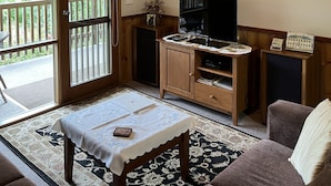 A living room with a wooden ceiling, a television, a small cabinet, a table with a white tablecloth, and a couch.