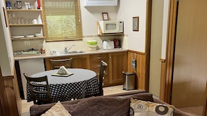 A compact living space with a kitchenette, a sofa with patterned cushions, a dining table, and a small trash bin.