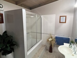 A bathroom with a glass-enclosed shower, a sink, and a framed notice on the wall.