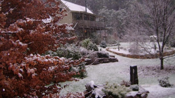 A house with a snow-covered roof and a yard with a wooden fence.
