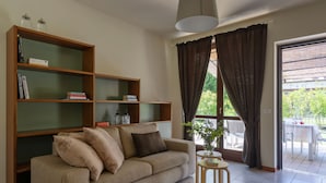 Een woonkamer met een bank, een boekenkast, een bijzettafeltje en een raam met gordijnen.