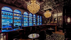 Eine Bar mit mehreren Flaschenregalen, einer Kristallleuchtre und einem gemusterten Boden.