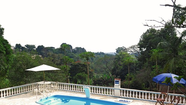 A swimming pool with a white fence, two umbrellas, and a view of a lush green landscape. - HOUSE, FARM, SITE, VERY GREEN 60 KM FROM SPAULO  (Santa Isabel)