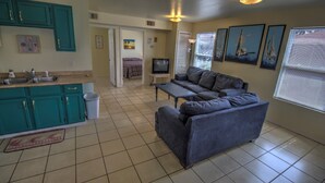 A compact living space with a kitchenette, a sofa, a television, and artwork on the walls. - Oleander Beach Lodge - Four Condos for One Great Price (South Padre Island)
