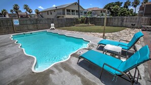 A swimming pool with a wavy edge, surrounded by a concrete deck. There are three blue lounge chairs and a small table. - Oleander Beach Lodge - Four Condos for One Great Price (South Padre Island)