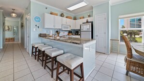 A kitchen with a central island, bar stools, white cabinets, and a refrigerator. - Just Steps to The Beach, Surrounded by Nature – TAKING SNOWBIRD BOOKINGS NOW! (Orange Beach)