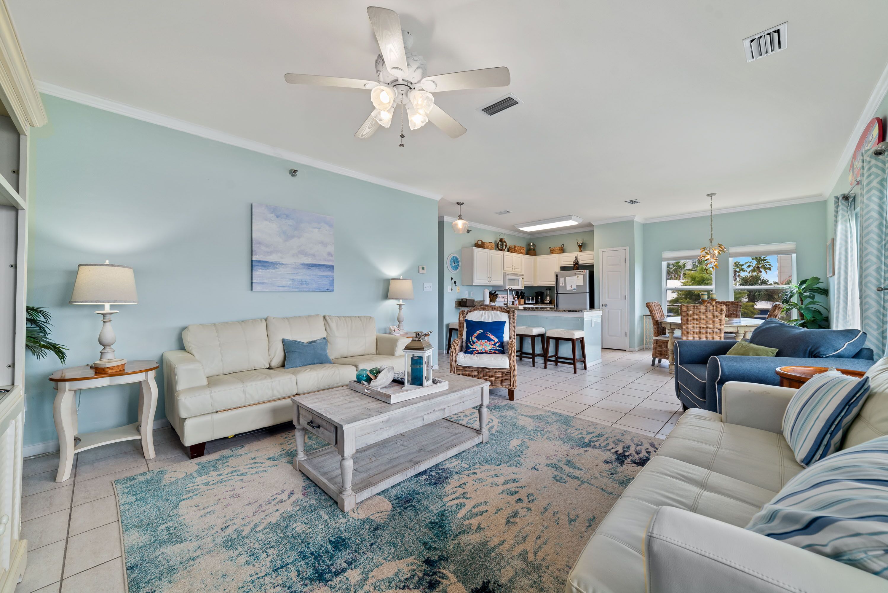 A spacious living room with a white sofa, a blue sofa, a wooden coffee table, and a ceiling fan.