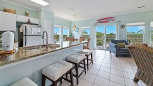 A modern kitchen with a bar area, white cabinets, and a view to the outside. - Just Steps to The Beach, Surrounded by Nature – TAKING SNOWBIRD BOOKINGS NOW! (Orange Beach)