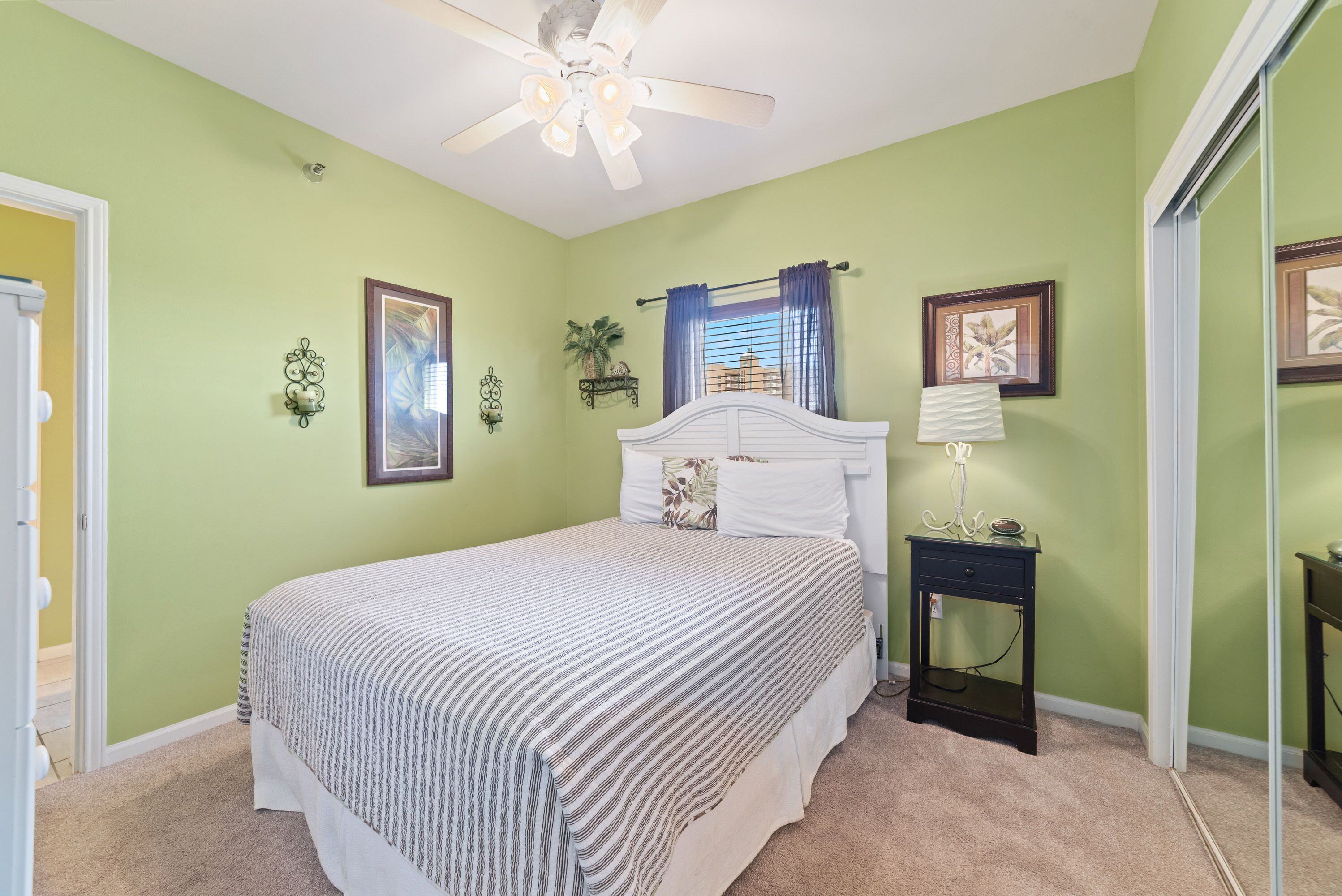 A bedroom with a bed, a ceiling fan, a nightstand, and a window with curtains.