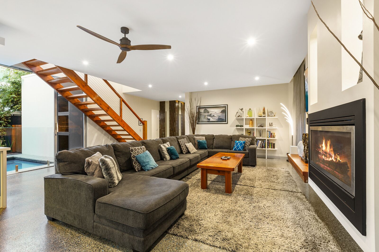 Una sala de estar moderna con un sofá modular, una mesa de centro, una chimenea, una estantería y una escalera.