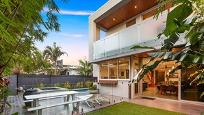 Une maison moderne à deux étages, dotée d’un balcon en verre, d’une piscine et d’une pelouse bien entretenue.