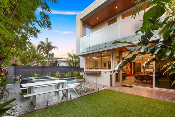 Une maison moderne à deux étages, dotée d’un balcon en verre, d’une piscine et d ’une pelouse bien entretenue.