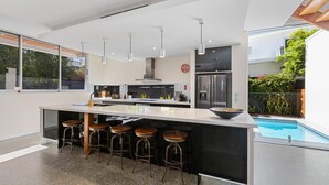 Une cuisine moderne dotée d’un îlot central, de tabourets de bar, d’appareils électroménagers en acier inoxydable et offrant une vue sur une piscine.