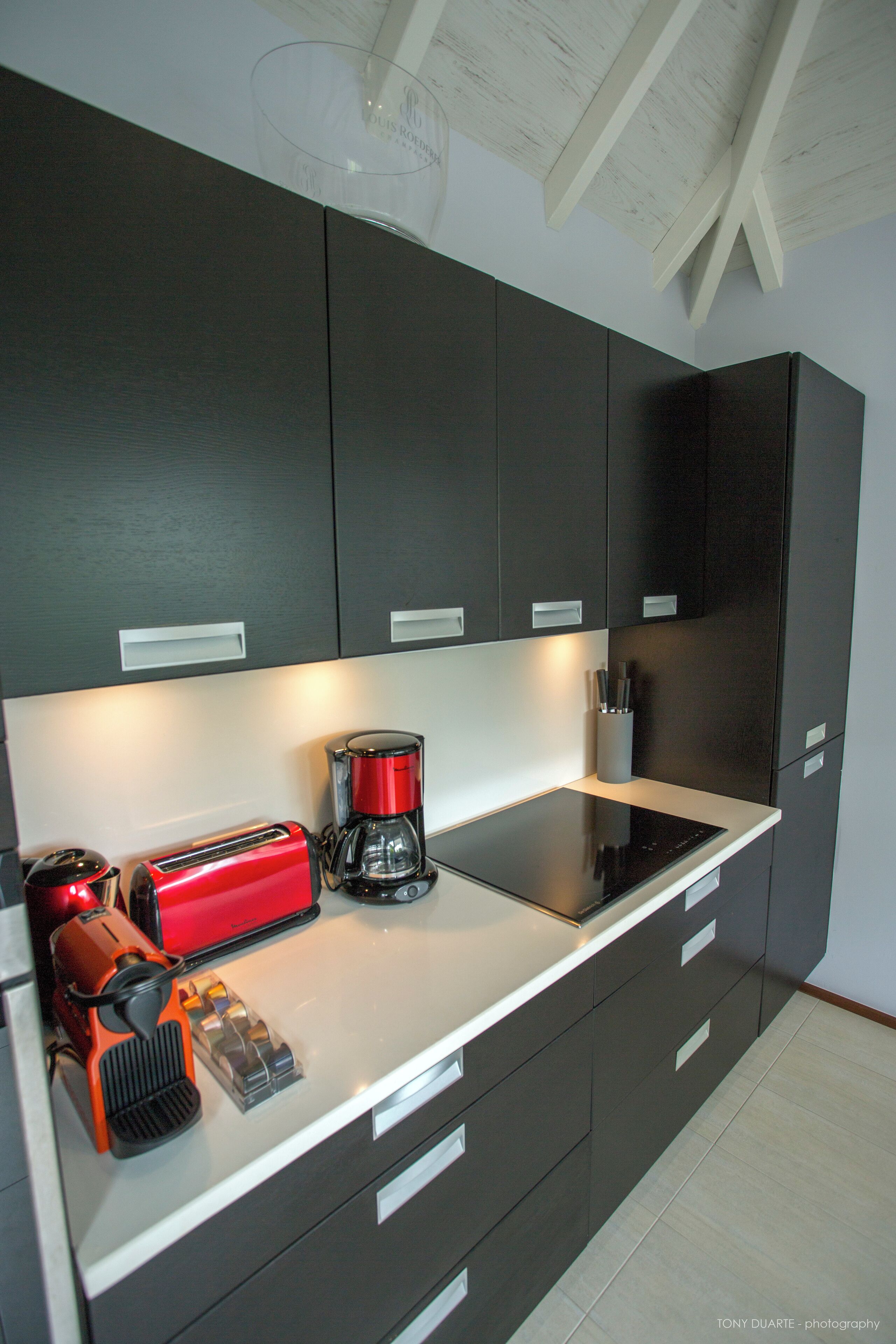 Een moderne keuken met donkere kastjes, een wit aanrecht en een koffiezetapparaat.