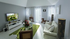 Una sala de estar moderna con una televisión de pantalla plana, un sofá blanco, una mesa de centro de vidrio y una lámpara de pie con forma de globo decorativo.