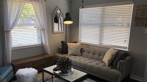 A living room with a sofa, ottoman, coffee table, and a decorative plant. - Beautiful Updated/Decorated Quaint Cottage in the Heart of Fredericksburg (Fredericksburg)