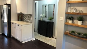 A modern kitchen with white cabinets, a black refrigerator, and a herringbone backsplash. There are wooden shelves with plants and a mirror above them. - Beautiful Updated/Decorated Quaint Cottage in the Heart of Fredericksburg (Fredericksburg)