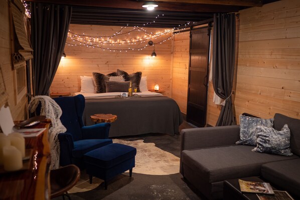 A cozy room with a bed, blue armchair, and a sofa. There are string lights and a small table with a bottle. - The Shed for Couples Only!-Hermann (Hermann)