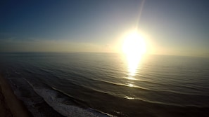 A beach with waves and a bright sun in the sky.