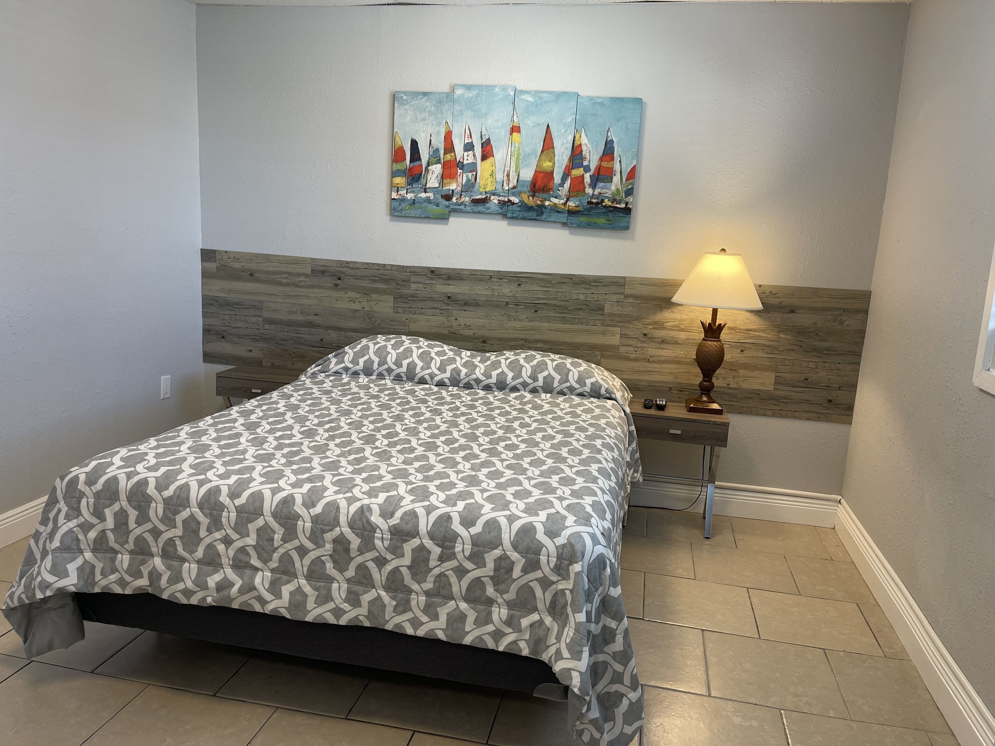A bedroom with a bed, a nightstand with a lamp, and a painting of sailboats on the wall.