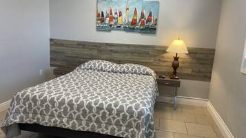 A bedroom with a bed, a nightstand with a lamp, and a painting of sailboats on the wall.