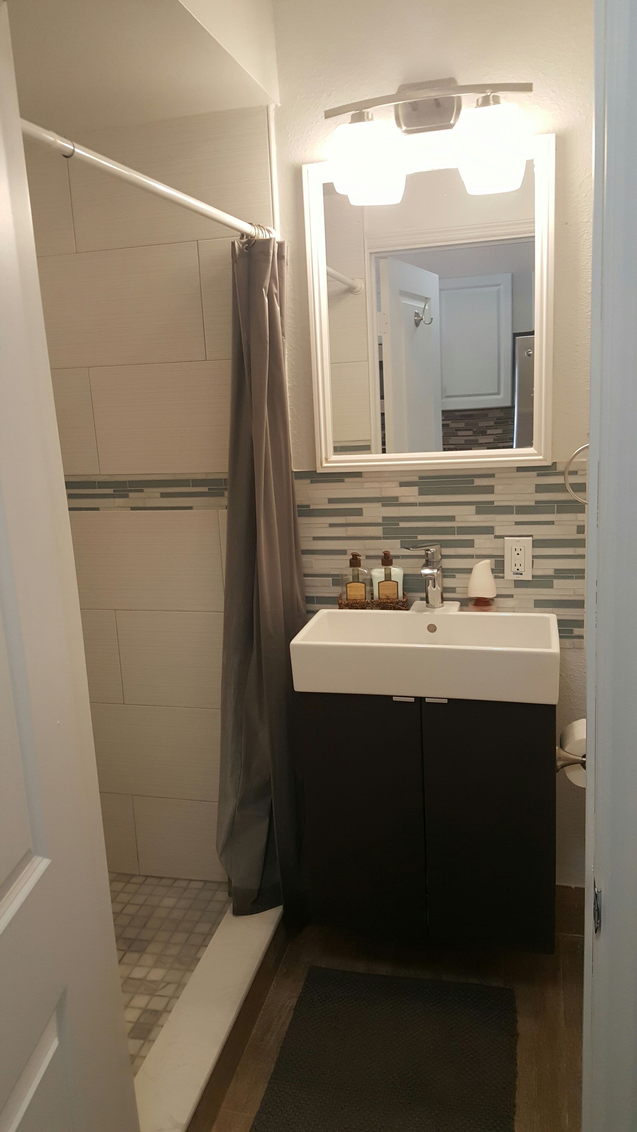 Een badkamer met een douche, een wastafel, een spiegel en een handdoekrek.