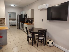 A compact kitchen with a dining area, a TV mounted on the wall, and a soccer ball on the floor. - NEW Apartment  Right Across the Street! With Parking Included! (Indialantic)