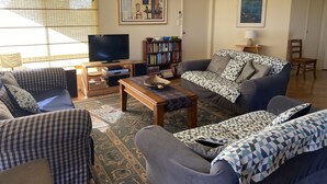 Una sala de estar con sofá, sillones, una mesa de centro, televisor, estantería y un cuadro en la pared.