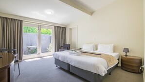 Ein Hotelzimmer mit Bett, Nachttischen, einem Schreibtisch und Blick auf Grün durch das Fenster.