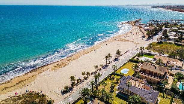 A coastal property with a beach, a swimming pool, and a road leading to the beach.