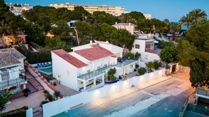 A coastal hotel with a red-tiled roof, multiple balconies, and a swimming pool.