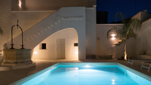 Una piscina con una escalera que lleva a una puerta, rodeada de paredes blancas y una palmera.
