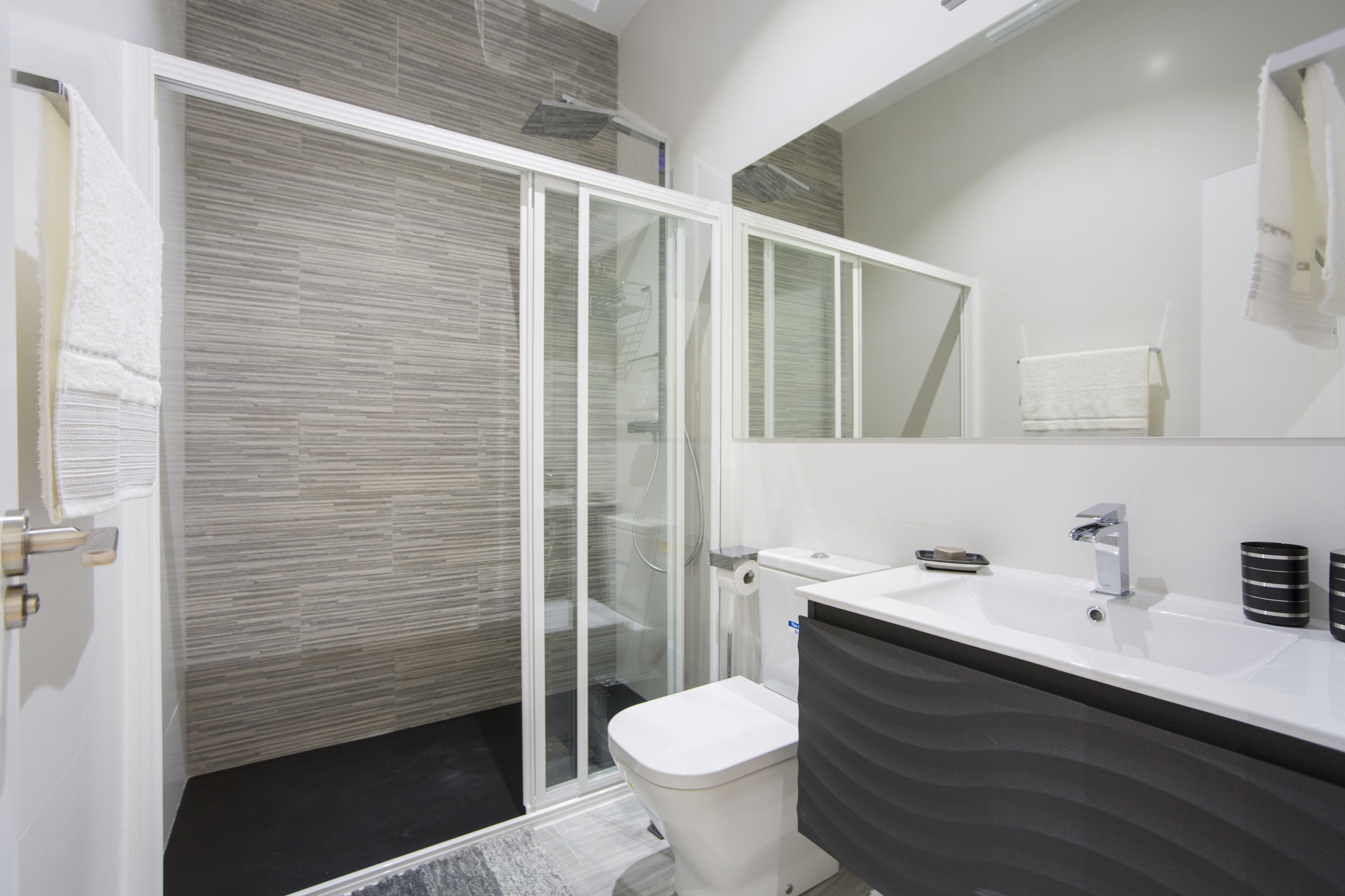 A modern bathroom with a glass shower enclosure, a white sink, and a large mirror.