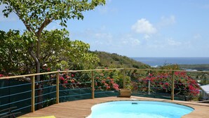 Une piscine avec une terrasse en bois, des chaises colorées et une vue sur l’océan.