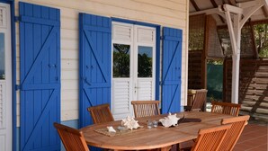 Une table en bois, des chaises et une porte blanche avec des volets bleus.