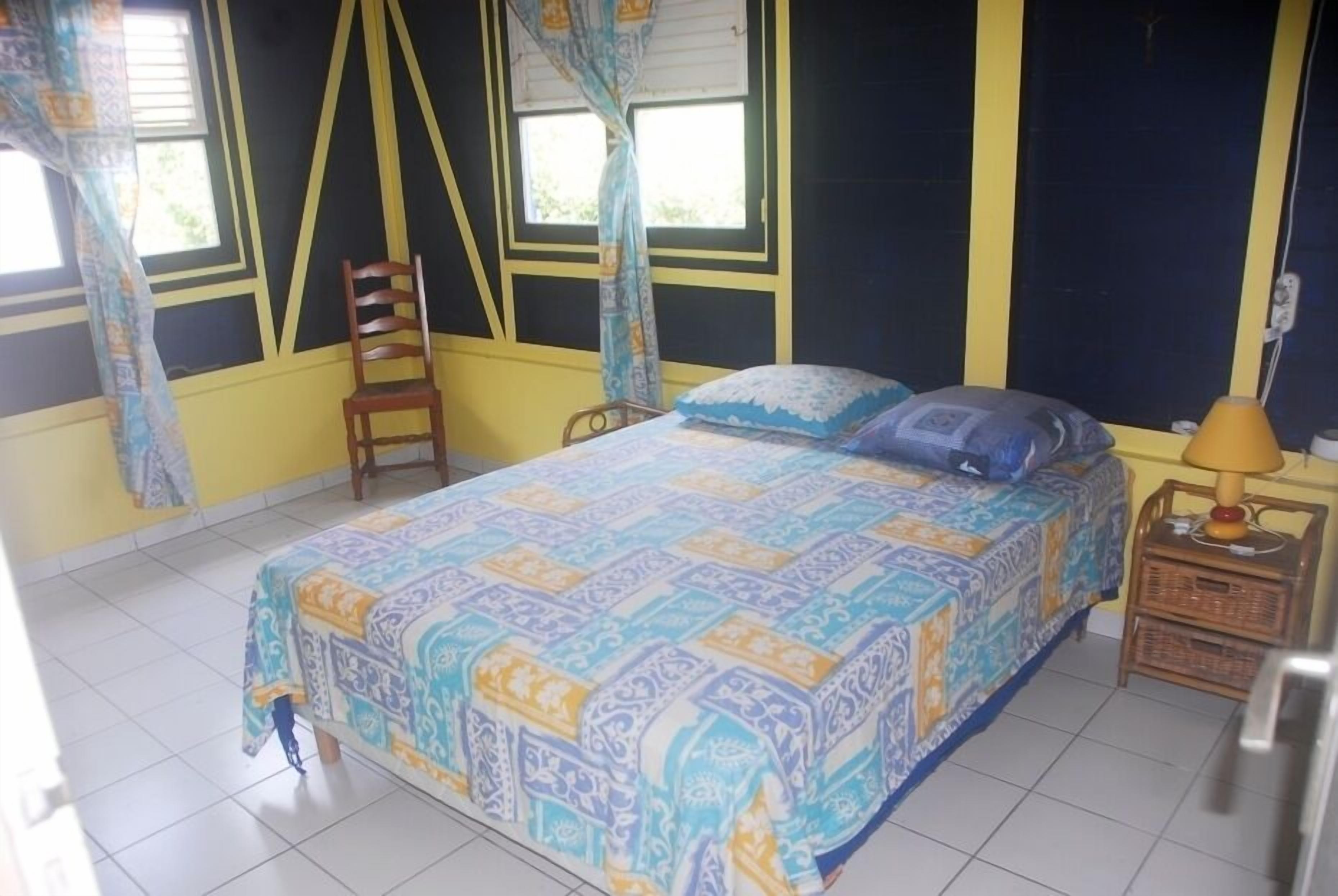 Een slaapkamer met een bed, een stoel, een nachtkastje en een raam met gordijnen.