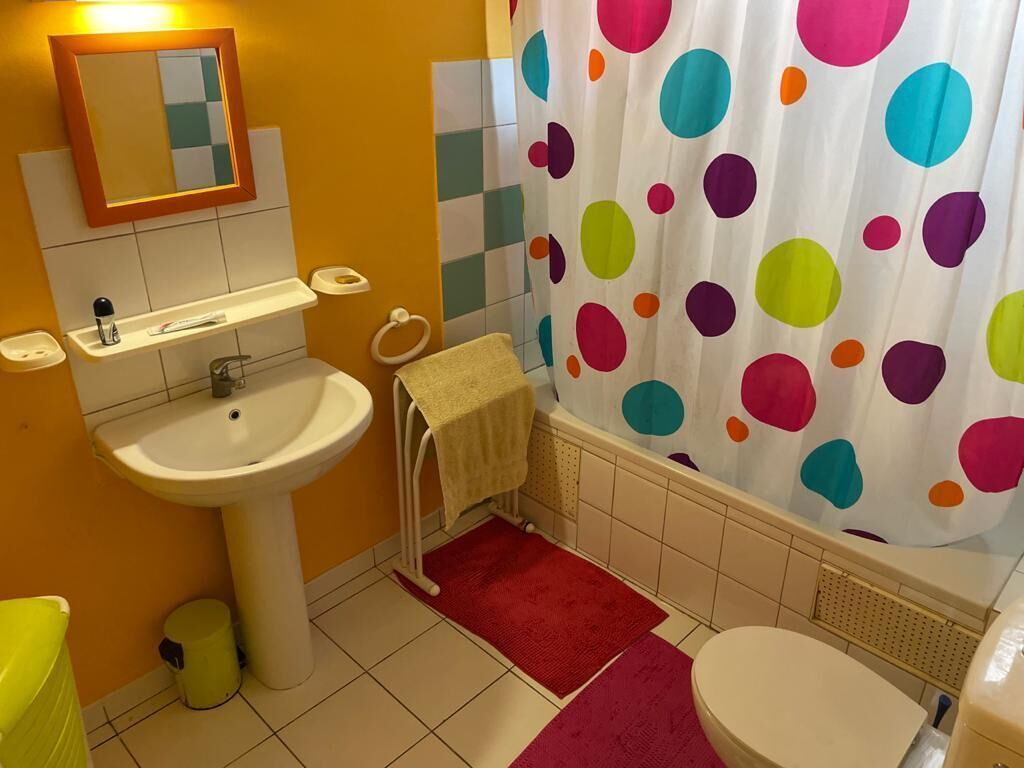 Un baño con un lavamanos blanco, un espejo, un perchero para toallas, un inodoro y una cortina de ducha con lunares de colores.