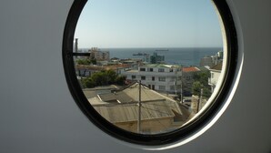 Vista a través de una ventana de un paisaje urbano costero con edificios y el mar.