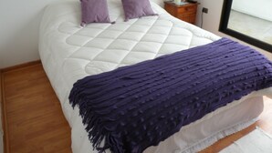 Una cama con colchón blanco acolchado, dos almohadas moradas y una manta morada.