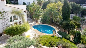 Zona residencial amb piscina envoltada de vegetació abundant, edificis blancs i un paisatge de pendent.