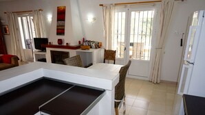 Una cuina moderna amb zona de menjador, armaris blancs i una finestra gran amb cortines.