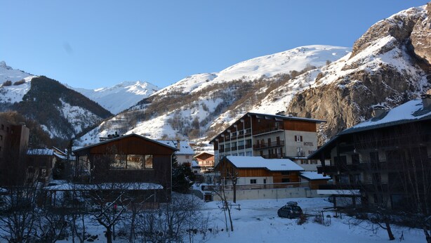 Ein verschneites Bergdorf mit Holzhäusern und einem Hotel namens "Hotel Bar".
