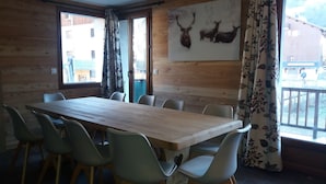 Ein Zimmer mit Holzwandverkleidung, einem großen Tisch mit Stühlen, Hirschbild an der Wand und Blick auf ein Gebäude.
